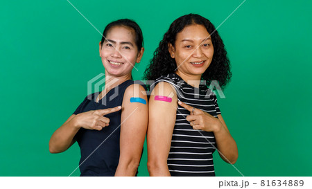Two middle aged Asian women showing their arms with bandage patch showing they got vaccinated for Covid 19 virus on green background. Concept for Covid 19 vaccination Two middle aged Asian women showing their arms with bandage patch showing they got vaccinated for Covid 19 virus on green background. Concept for Covid 19 vaccination 81634889