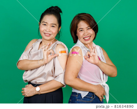 Two middle aged Asian women showing their arms with bandage patch showing they got vaccinated for Covid 19 virus on green background. Concept for Covid 19 vaccination Two middle aged Asian women showing their arms with bandage patch showing they got vaccinated for Covid 19 virus on green background. Concept for Covid 19 vaccination 81634890