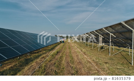 Top view of specialists walking across a solar power plant. Three employees of alternative power plant walking and talking about scheme of solar panels. Teamwork. Group of specialists. Top view of specialists walking across a solar power plant. Three employees of alternative power plant walking and talking about scheme of solar panels. Teamwork. Group of specialists. 81635379