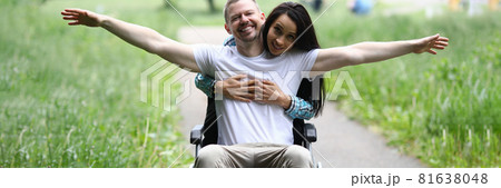 Woman hugs joyful man in wheelchair in park Woman hugs joyful man in wheelchair in park 81638048