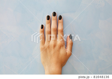 Nails with a beautiful black manicure with glitter on a female hand on a marble background of a blue wall in blur. 81648136