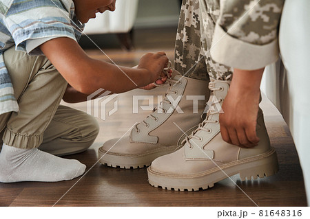 Woman wearing military uniform sitting at the sofa while her son tie her shoe laces Woman wearing military uniform sitting at the sofa while her son tie her shoe laces 81648316