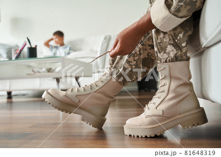 Woman wearing military uniform tie her shoe laces while sitting at the sofa 81648319