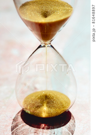 Sand running through the bulbs of an hourglass measuring the passing time in a countdown to a deadline, on a light pastel reddish background Sand running through the bulbs of an hourglass measuring the passing time in a countdown to a deadline, on a light pastel reddish background 81648897