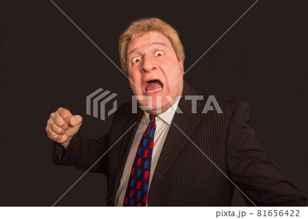 Studio shot of angry senior businessman with fist raise against dark background Studio shot of angry senior businessman with fist raise against dark background 81656422