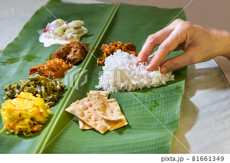 Person enjoying Indian banana leaf rice consisting mutton curry, squid, prawn, papadam and various vegetables 81661349