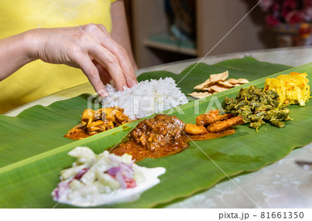 Person enjoying Indian banana leaf rice consisting mutton curry, squid, prawn, papadam and various vegetables 81661350