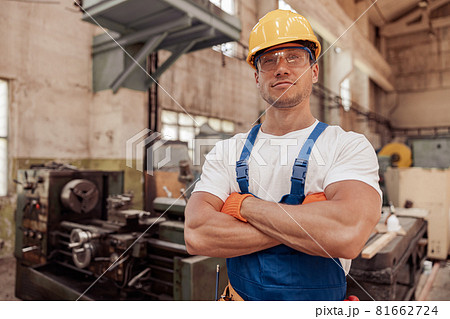 Athletic male builder in construction helmet standing in workshop Athletic male builder in construction helmet standing in workshop 81662724