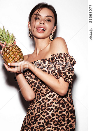 Beautiful sexy woman with pineapple in hands in a leopard dress and earrings, with classic smokey makeup and a fashionable hairstyle. Beauty face. Beautiful sexy woman with pineapple in hands in a leopard dress and earrings, with classic smokey makeup and a fashionable hairstyle. Beauty face. 81663077