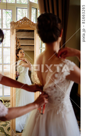 the bride is helped to put on a dress and fastened the corset. the bride is helped to put on a dress and fastened the corset. 81663265