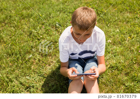 Outdoor portrait of blond boy teenager, male young man texting or using social media on cell phone on nature background. Summer, technology or people concept 81670379