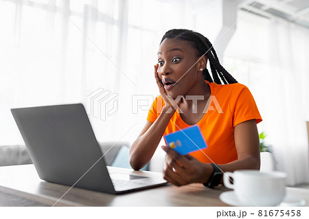 Emotional Afro lady looking at laptop screen, holding credit card, shocked over huge sale in web store 81675458