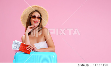 Positive Young Girl in straw hat and sunglasses With Tickets And Suitcase Pink Studio Background, smiles looking away 81676196