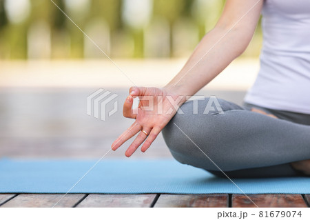 Cropped shot of female sitting on lotus pose on mat and meditating during yoga outdoor class Cropped shot of female sitting on lotus pose on mat and meditating during yoga outdoor class 81679074