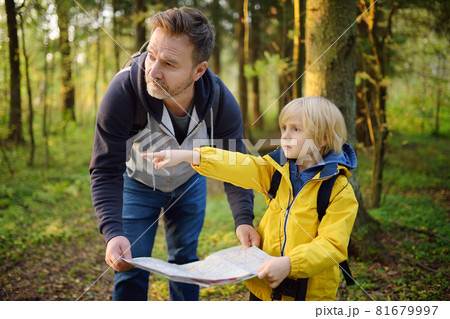 Schoolchild and his mature father hiking together and exploring nature. Little boy with dad looking map during orienteering in forest. Adventure, scouting and hiking tourism for kids. Schoolchild and his mature father hiking together and exploring nature. Little boy with dad looking map during orienteering in forest. Adventure, scouting and hiking tourism for kids. 81679997