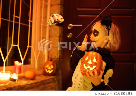 Little child in scary skeleton costume at Halloween celebration party. The child is ready for trick or treat on Halloween night. The kid scares big silver hand appearing from behind the door. 81680293