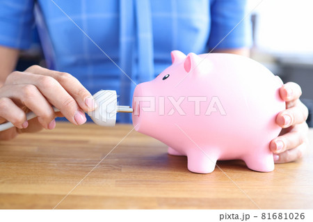 Woman is holding electrical plug and and pink piggy bank closeup 81681026
