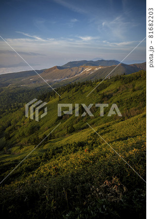 朝の太陽に照らされて輝く峠の草原と山の向こうに青空が広がる 81682203