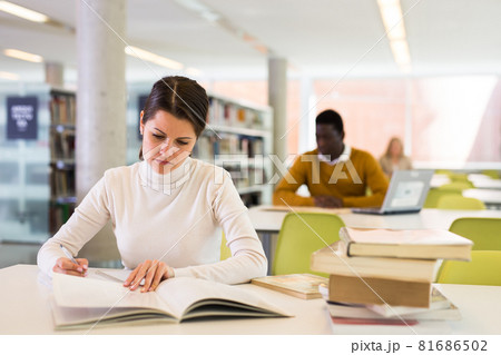 Portrait of confident woman with book in public library Portrait of confident woman with book in public library 81686502