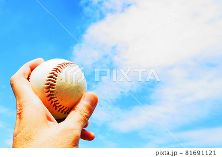 青空の下 野球ボールを握り持ち上げる手の写真素材