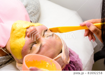 Applying a gold mask on a woman's face, a procedure in a beauty salon. 81692258