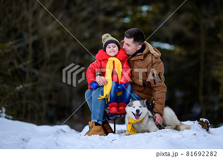 A father with a beautiful daughter and a husky dog are walking in the winter forest. 81692282