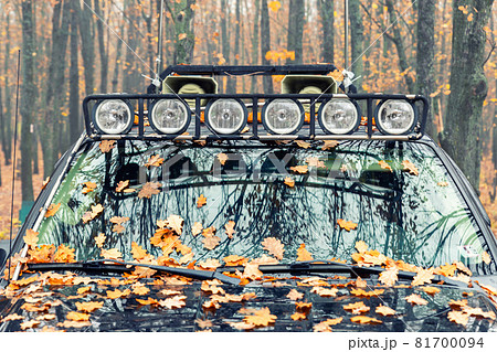 Close-up detail view of custom made roof rack bar with extra headlight mounted on roof of heavy duty pick up suv car against foggy autumn forest. Fallen leaves vehicle windshield. Fall weather drive Close-up detail view of custom made roof rack bar with extra headlight mounted on roof of heavy duty pick up suv car against foggy autumn forest. Fallen leaves vehicle windshield. Fall weather drive 81700094