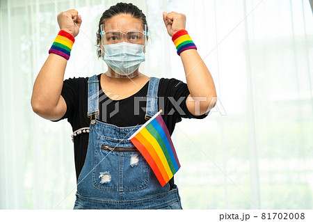 Asian lady wearing blue jean jacket or denim shirt and holding rainbow color flag, symbol of LGBT pride month celebrate annual in June social of gay, lesbian, bisexual, transgender, human rights. 81702008