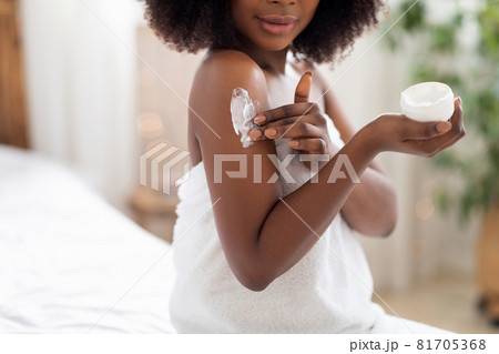 Unrecognizable black lady applying body cream on shoulder after shower in morning at home Unrecognizable black lady applying body cream on shoulder after shower in morning at home 81705368