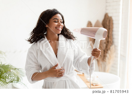 African Female Drying Hair Using Hairdryer Enjoying Haircare Routine Indoors 81705943