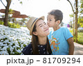 The little son kissed his mother's cheek, who was smiling happily in the beautiful flower garden. 81709294