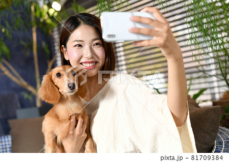 ペット 犬 とスマートフォンで自撮りをする若い女性の写真素材