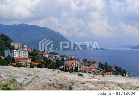 Aerial shot of cityscape with mountains in the background on a sunny day. View from the fortress over Herceg Novi, Montenegro, on the Bay of Kotor Aerial shot of cityscape with mountains in the background on a sunny day. View from the fortress over Herceg Novi, Montenegro, on the Bay of Kotor 81713604
