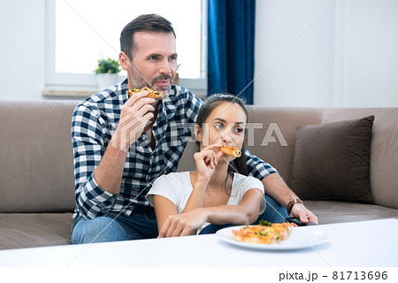 Couple watching TV while eating pizza Couple watching TV while eating pizza 81713696