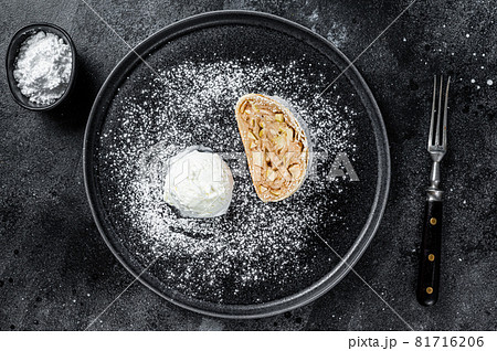 Apple strudel with cinnamon, powdered sugar and vanilla ice cream on a plate. Black background. Top view 81716206