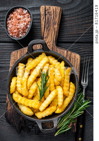 Fried Crinkle French fries potatoes in a pan. Black Wooden background. Top view 81716419