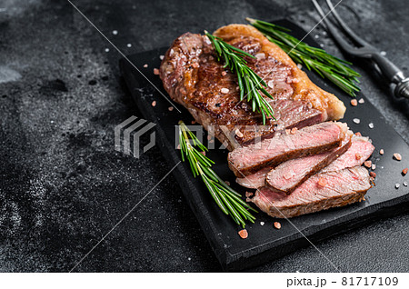 Cut roasted new york strip beef meat steak or striploin on a marble board. Black background. Top view. Copy space Cut roasted new york strip beef meat steak or striploin on a marble board. Black background. Top view. Copy space 81717109