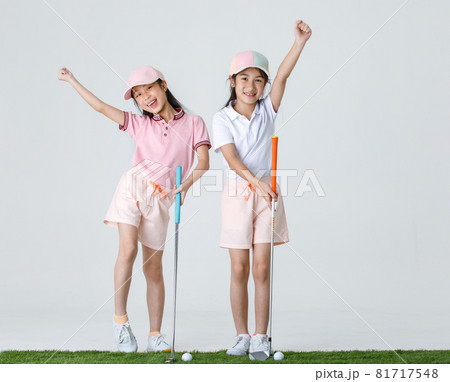 Portrait isolated studio shot of two Asian little professional girl golfers in  athlete fashion clothing stand smile hold fist up overhead when receive victory win in game in front white background 81717548