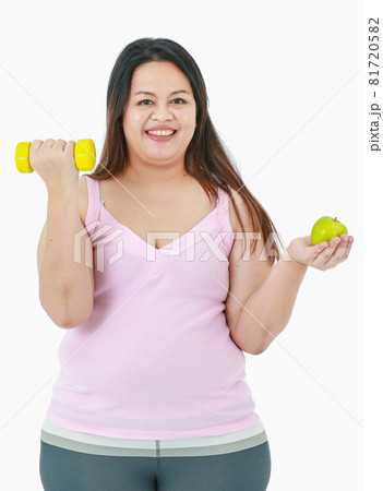 Portrait isolated studio shot of Asian happy healthy big fat oversize girl in sport clothing standing smiling lifting yellow dumbbell and hold organic green apple in other hand on white background 81720582