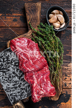 Raw machete skirt beef steak on butcher board with cleaver. Dark wooden background. Top view 81721060