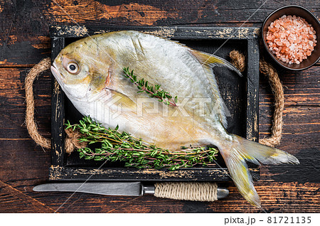 Raw fish butterfish or pompano with herbs in a wooden tray. Dark wooden background. Top view 81721135