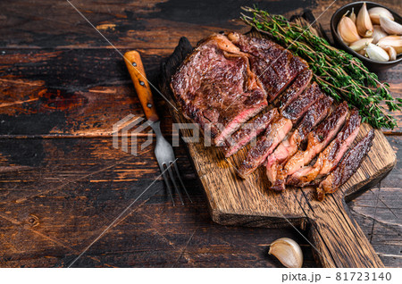 Roasted and sliced rib eye beef meat steak on a wooden cutting board with thyme. Dark wooden background. Top view. Copy space 81723140