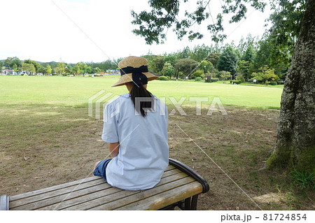広い公園のベンチに座った女の子の後ろ姿の写真素材