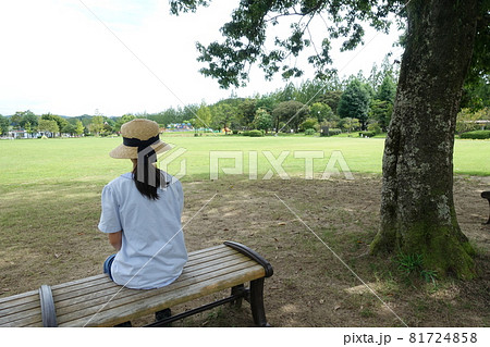 広い公園のベンチに座った女の子の後ろ姿の写真素材