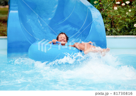 happy an 8 year old boy is riding in the water Park on inflatable circles on water slides with splash 81730816