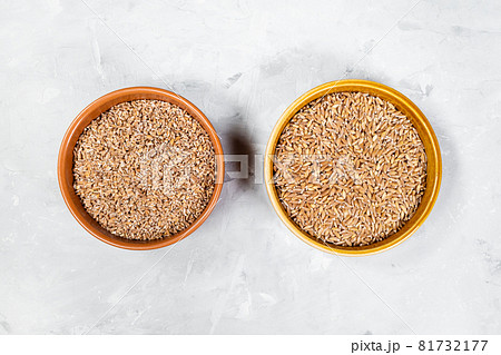 top view of crushed and whole Emmer farro hulled wheat grains in round ceramic bowls on gray concrete board 81732177