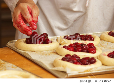Work in bakery, making fruit filled pies. The woman in the picture is making filled fruit pies. Hands filling pie yeast dough with strawberries. Work in the bakery. 81733652