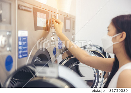 At a laundromat shop with many automatic washing machines, a beautiful woman wearing a mask is doing laundry. At a laundromat shop with many automatic washing machines, a beautiful woman wearing a mask is doing laundry. 81739080