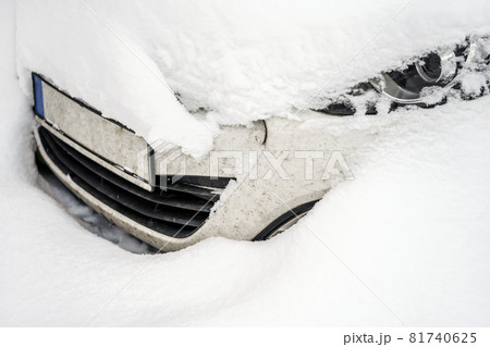 Car under deep layer of snow after heavy snowstorm, detail on only part of headlight and front bumper visible. Car under deep layer of snow after heavy snowstorm, detail on only part of headlight and front bumper visible. 81740625