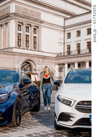 Beautiful woman between cars on parking place. The girl is standing between two cars. Beautiful woman between cars on parking place. The girl is standing between two cars. 81742856